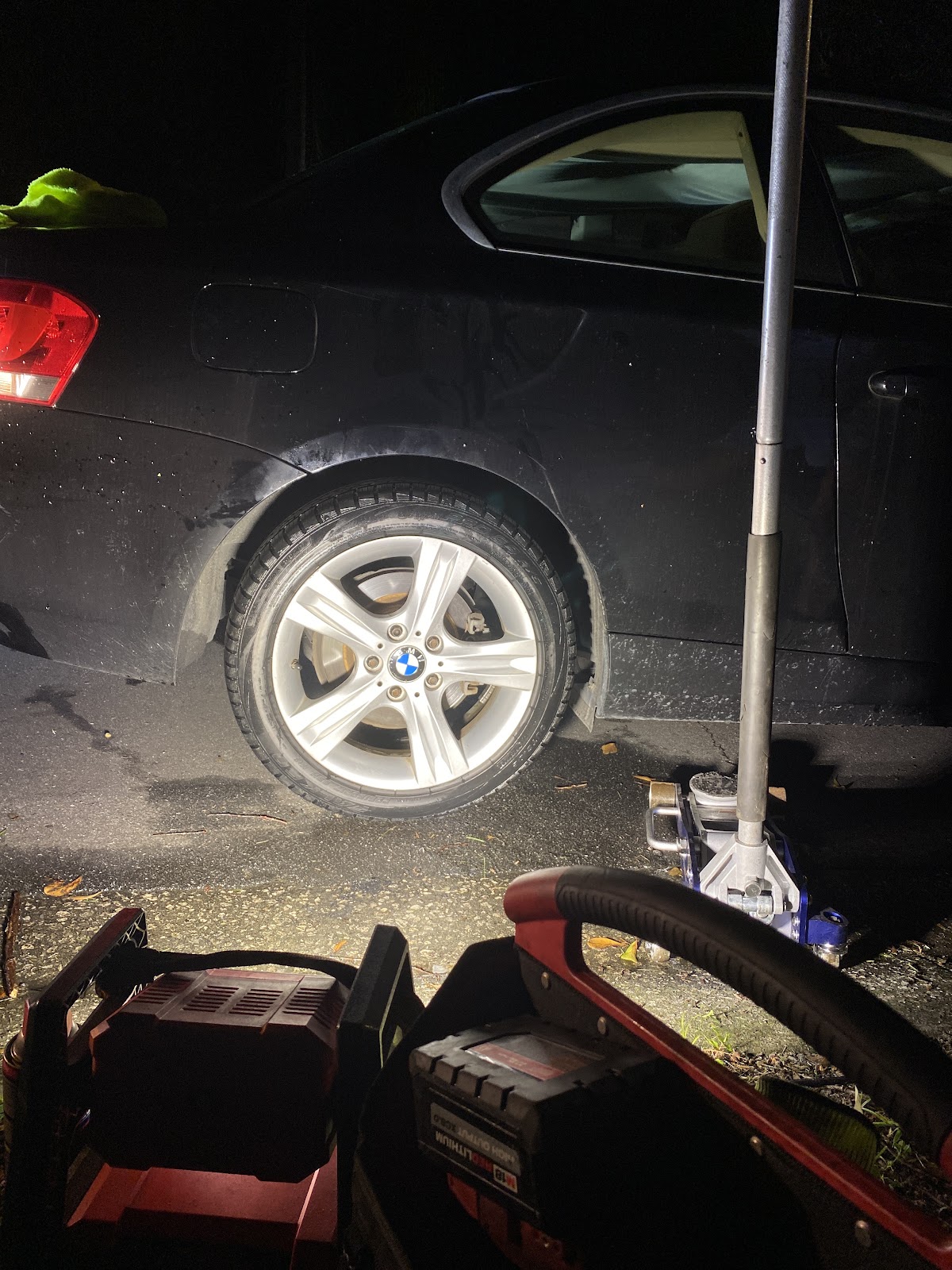 Tire & Ride Mobile — black BMW coupe during overnight roadside flat-tire service with floor jack staged